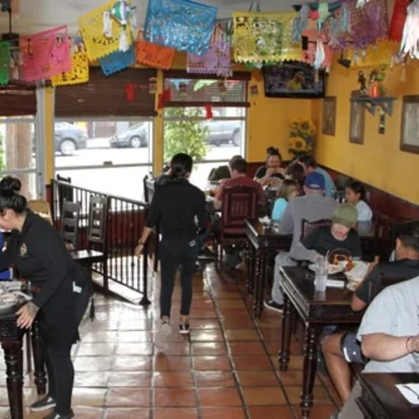 A vibrant Mexican restaurant interior with colorful papel picado, diners, and staff serving tables.