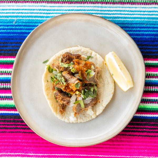 A single taco with meat, salsa, onions, and cilantro, with a lemon wedge on a plate.