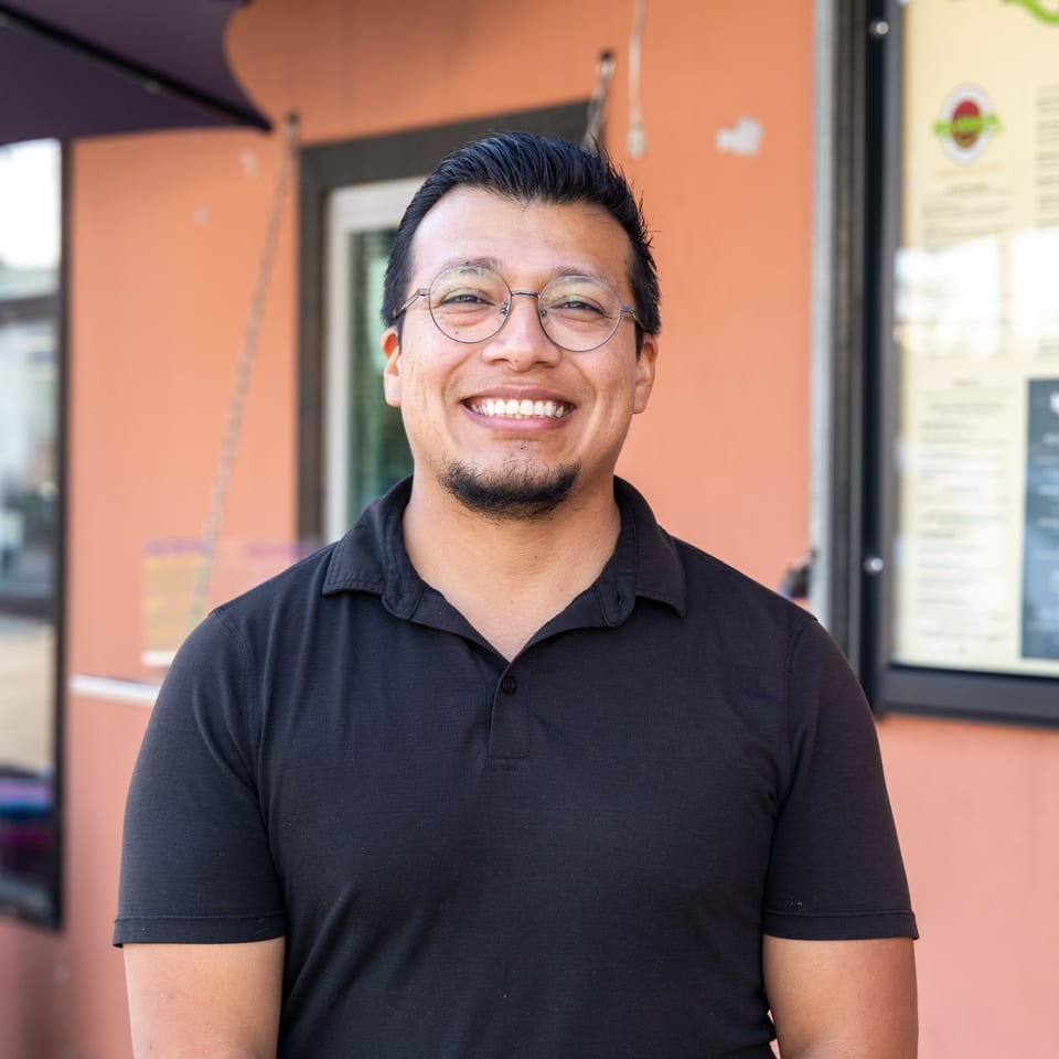 Smiling man in glasses and a black polo shirt standing outside a restaurant.