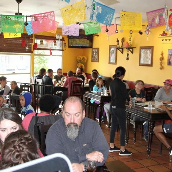 A busy restaurant interior with patrons seated at tables under colorful papel picado decorations.