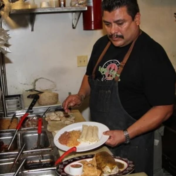Chef in a black apron preparing a plate of Mexican food with rice, beans, and tamales.