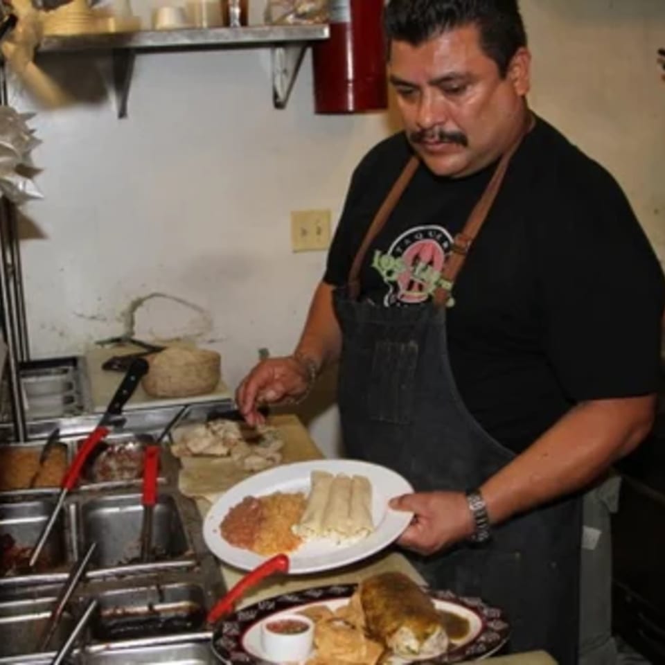 Chef in a black apron preparing a plate of Mexican food with rice, beans, and tamales.