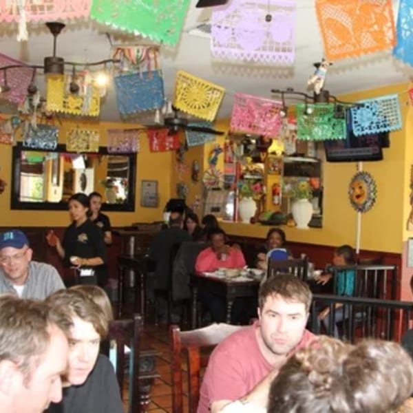 A vibrant Mexican restaurant interior with colorful papel picado banners, diners, and waitstaff.