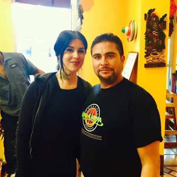 A man and woman pose for a photo in a brightly lit restaurant with yellow walls and decor.