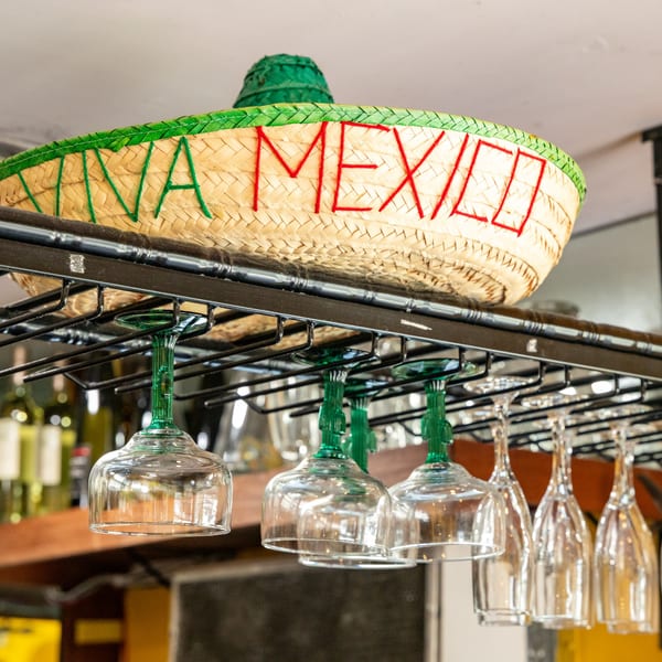 A straw sombrero with "VIVA MEXICO" embroidered on it, above hanging margarita and wine glasses.